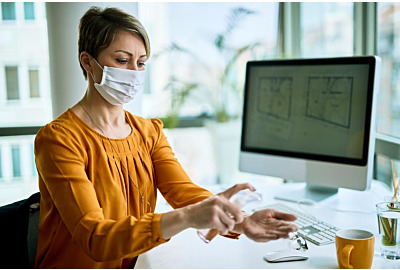 Geschäftsfrau mit Gesichtsmaske mit Handanisierer, während sie im Büro die Hände reinigt.